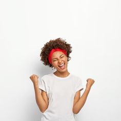 a woman with her arms in the air and smiling while standing against a white wall