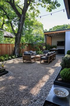 Modern backyard seating area with wooden furniture on a pea gravel patio, shaded by trees. Includes outdoor lighting and decor. Perfect for a backyard getaway. Backyard Landscaping Easy Maintenance, The Perfect Backyard, In Ground Patio Ideas, Outdoor Furniture On Gravel, Mulch Patio Ideas Backyards, Garden Design Gravel, Side Yard Pea Gravel, Low Maintenance Gravel Garden, Crushed Granite Backyard Ideas