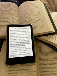 an open book sitting on top of a pile of books next to a smart phone