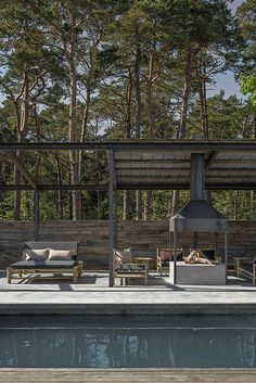 an outdoor living area next to a swimming pool with furniture on the deck and trees in the background