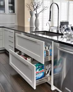 an open dishwasher in a kitchen with white cabinets and black counter tops,