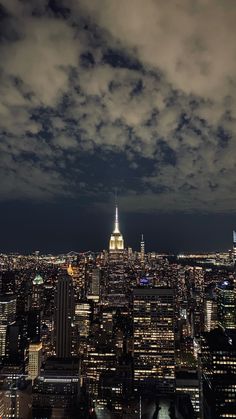 the empire building is lit up at night in new york city, ny with dark clouds overhead