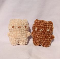 two small knitted animals sitting next to each other on a white surface, one is brown and the other is beige