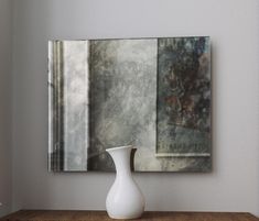 a white vase sitting on top of a wooden table in front of a framed painting