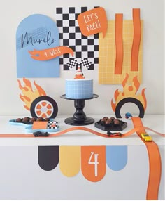 a table topped with a cake covered in frosting next to race flags and other decorations