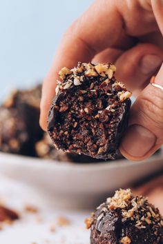 a person is holding a piece of chocolate cake in front of a bowl full of nuts