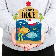 a person holding up a box with fish on it that says fishing hole in front of them