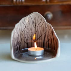 a lit candle sitting on top of a table next to a wooden box with drawers