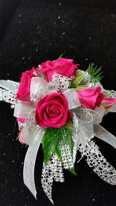 a pink rose and white ribbon corsage on a black surface with sequins