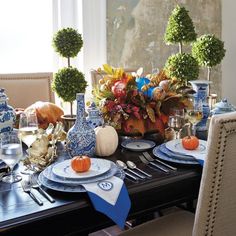 a dining room table is set with blue and white dishes, pumpkins, vases and flowers