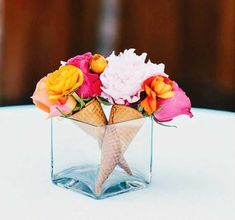 an ice cream cone with flowers in it on top of a white tablecloth covered table