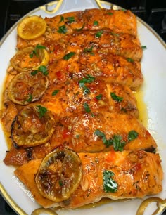 a white plate topped with fish covered in sauce and sliced lemons on top of it