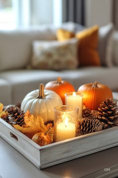 a tray filled with candles and pumpkins on top of a table next to a couch