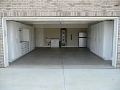 an empty garage with two refrigerators and cabinets in the door way, next to a brick wall