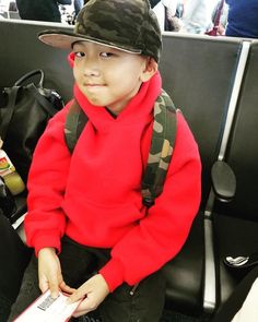 a young boy wearing a red sweater and camo hat sitting in an airport seat