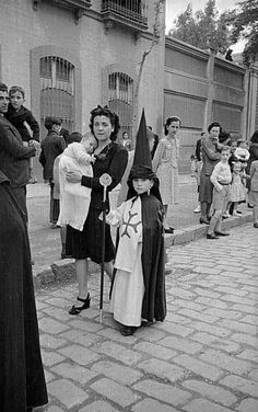 an old black and white photo shows people dressed in costumes, standing on the sidewalk