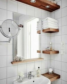 a white sink sitting under a bathroom mirror next to a wooden shelf filled with towels