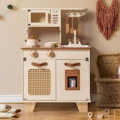 a toy kitchen set sitting on top of a hard wood floor next to a wicker chair