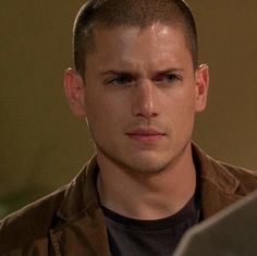 a young man looking at the camera while wearing a brown shirt