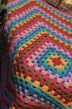 a colorful crocheted blanket sitting on top of a wooden chair next to a potted plant