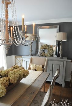 a chandelier hangs over a dining room table with flowers and candles on it