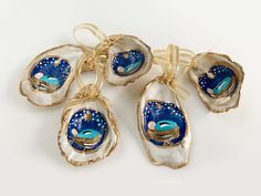 six seashells with blue and white designs are tied to gold ribbons on a white surface