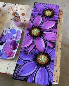 an artist's palette with paint and flowers on the table next to her easel