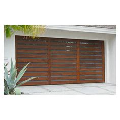 a wooden garage door in front of a white house with an aloen plant