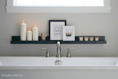 a bathroom with candles and pictures on the shelf above the bathtub, along with other decor items