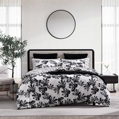 a bed with black and white comforters in a room next to a plant on the floor