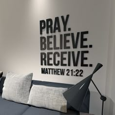 a couch with pillows and a lamp in front of a wall that says pray believe receive