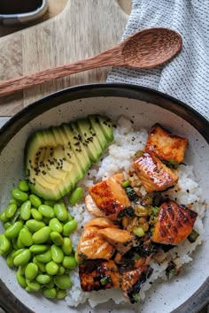 a bowl filled with rice, meat and vegetables next to a wooden spoon on top of a table