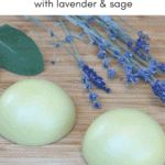 two green apples sitting on top of a wooden cutting board next to lavender and sage