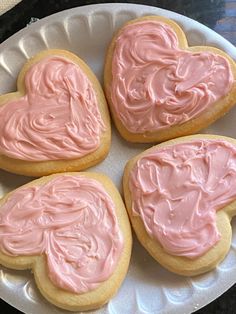 four heart shaped cookies with pink frosting on a plate