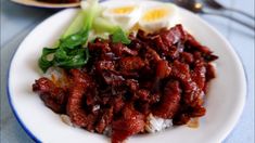 a white plate topped with meat and rice next to an egg on top of a table