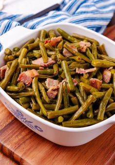 green beans with bacon in a white dish on a wooden cutting board next to a blue and white towel