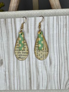 a pair of green and yellow polka dot tear shaped earrings hanging from a wooden frame