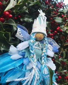 a blue and white christmas angel ornament hanging from a tree with red berries