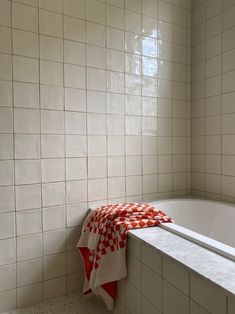 a bath tub sitting next to a window in a white tiled bathroom with red and white checkered towels on the edge