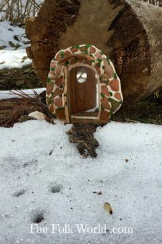 a small wooden door sitting in the snow next to a tree stump and logs with green leaves on it