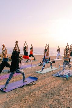 a group of people are doing yoga on the beach at sunset with their hands in the air