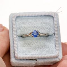 a person holding an engagement ring with a blue stone in it's middle finger