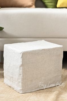 a white ottoman sitting on top of a wooden floor next to a couch and pillows