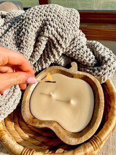 a person lighting a candle in a wooden bowl on a table next to a blanket