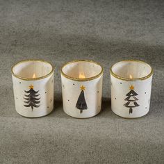 three white candles with gold trim decorated with christmas trees and stars, on a gray background