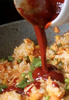 someone is pouring sauce on some food in a bowl with rice and beans, as well as peas