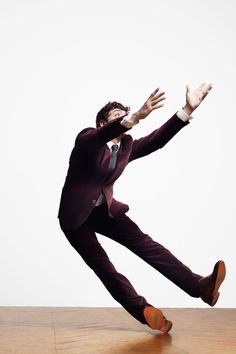 a man in a suit and tie is jumping on a wooden floor with his arms outstretched