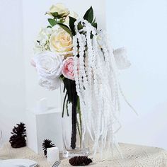 a vase filled with white and pink flowers on top of a table next to pine cones