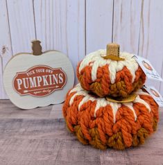 two orange and white knitted pumpkins sitting on top of each other next to a sign