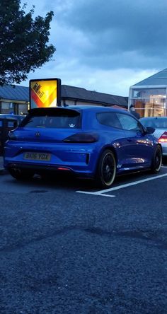 a blue car parked in a parking lot next to a building with a yellow sign on it's side